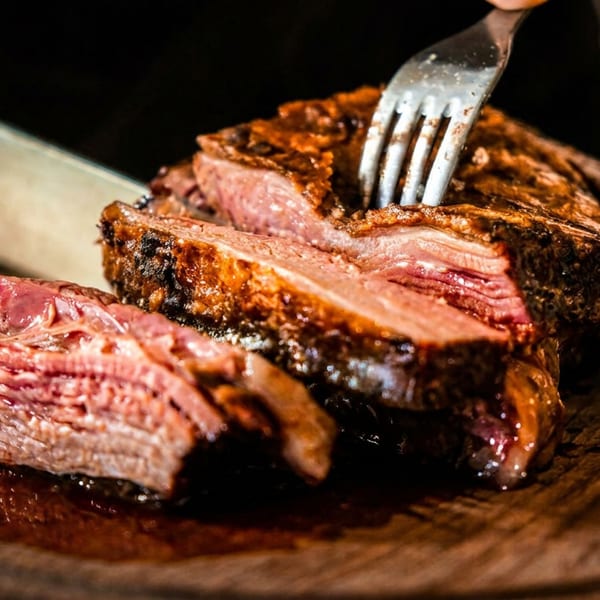 Hand cutting juicy, grilled meat with a knife and fork on a wooden board.