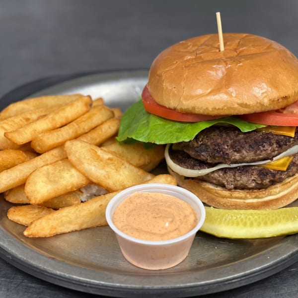 Double cheeseburger with lettuce, tomato, onion, fries, dipping sauce, and pickle spear on a plate.