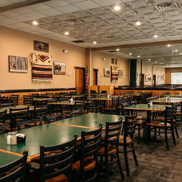 Spacious restaurant dining room with green-topped tables, dark chairs, and decorative wall art.
